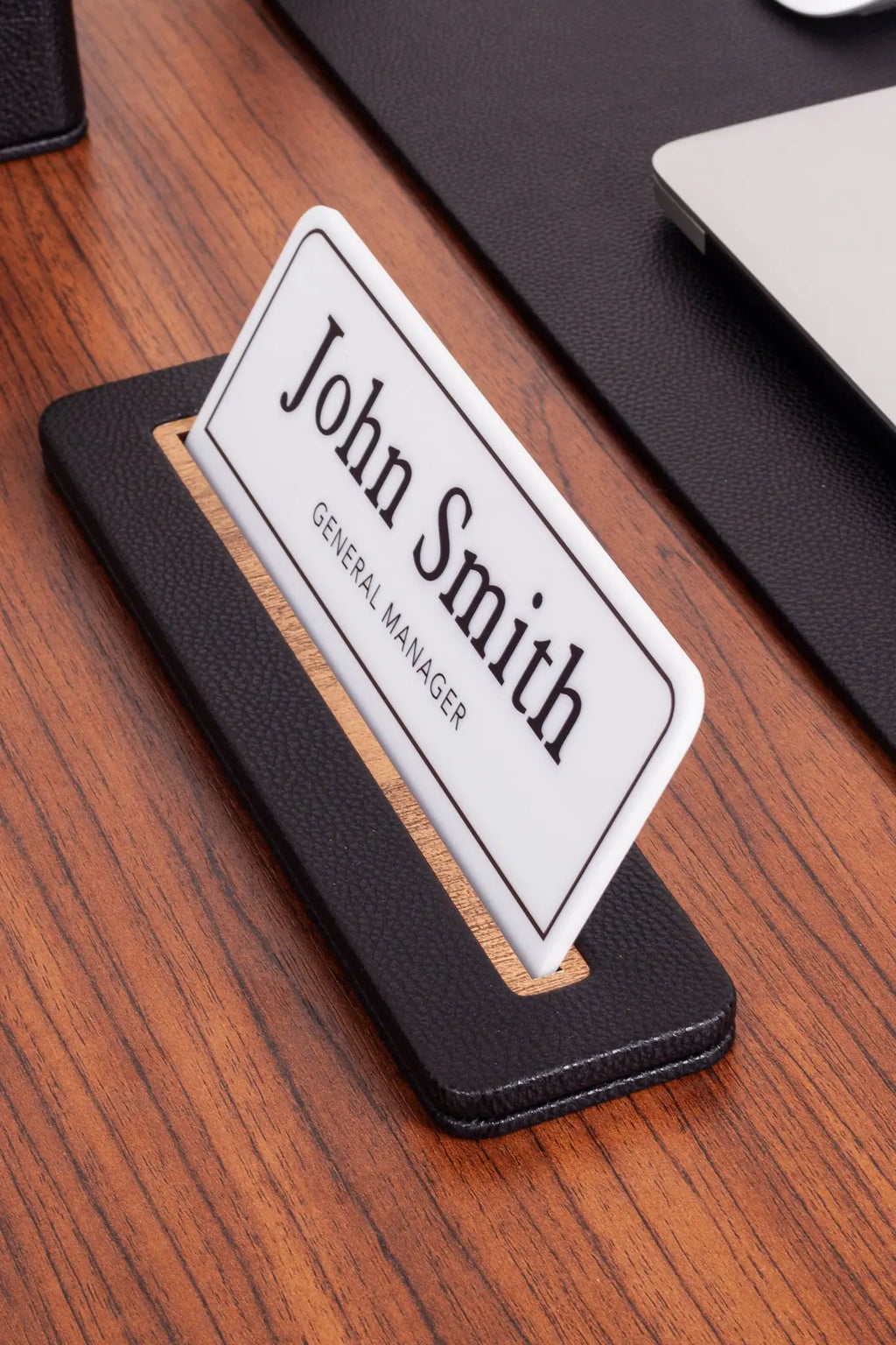 Siyah deri masa isimliği, ahşap detay ile desteklenmiş, beyaz arka planda "John Smith" yazılı.